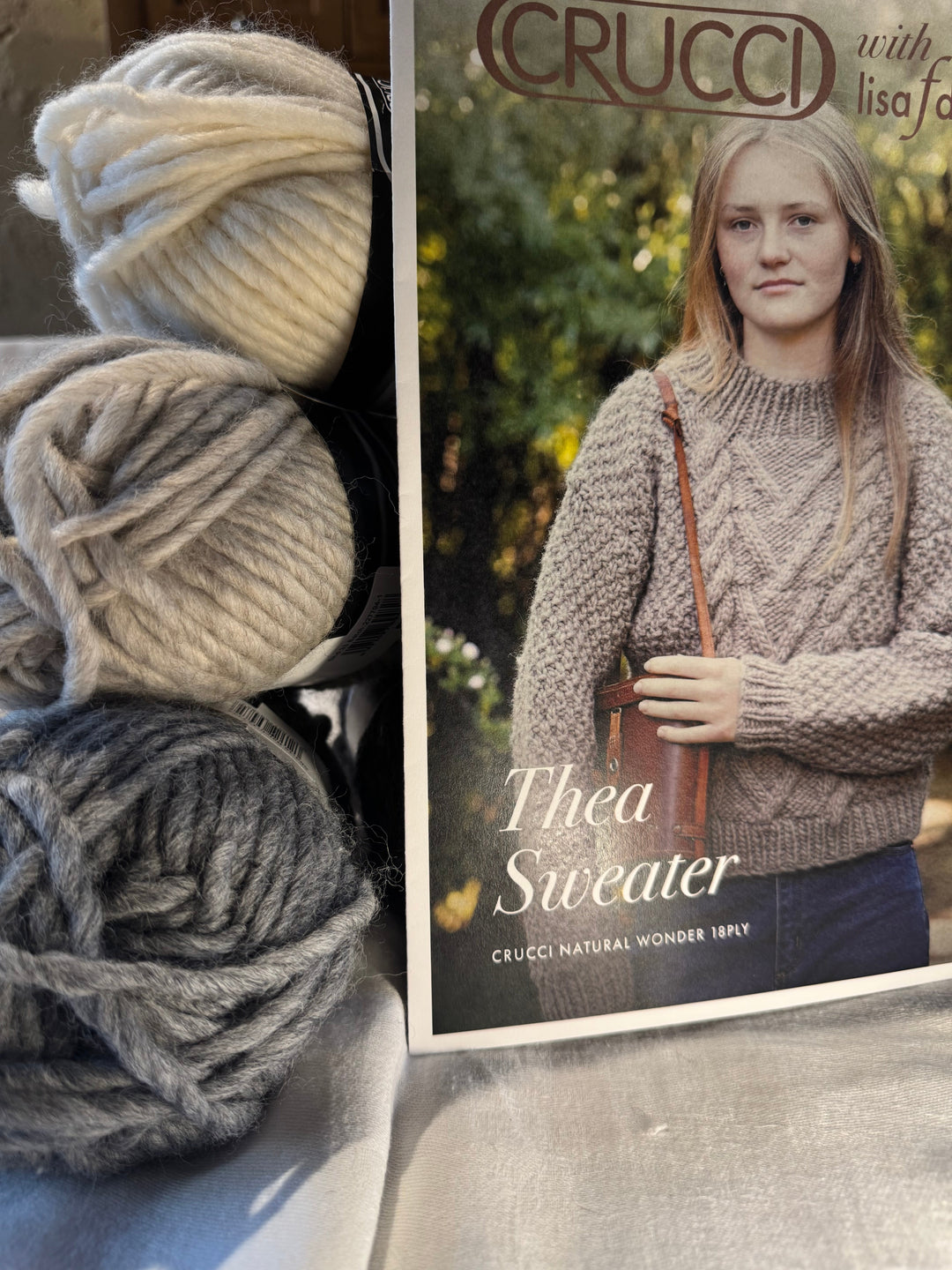 A knitter reading a knitting pattern with yarn and needles nearby