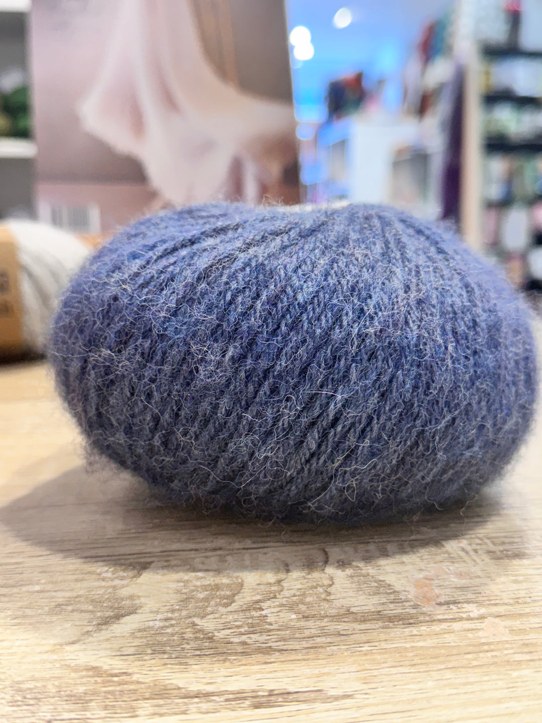 Blue alpaca yarn ball on a wooden surface with a blurred indoor background