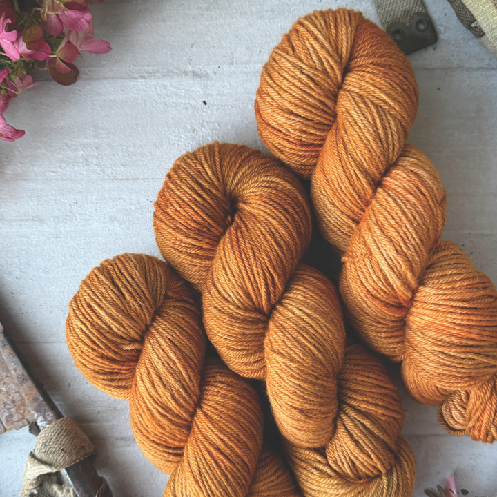 Orange yarn skeins from Yarn Phase on a textured surface with flowers and tools in the background