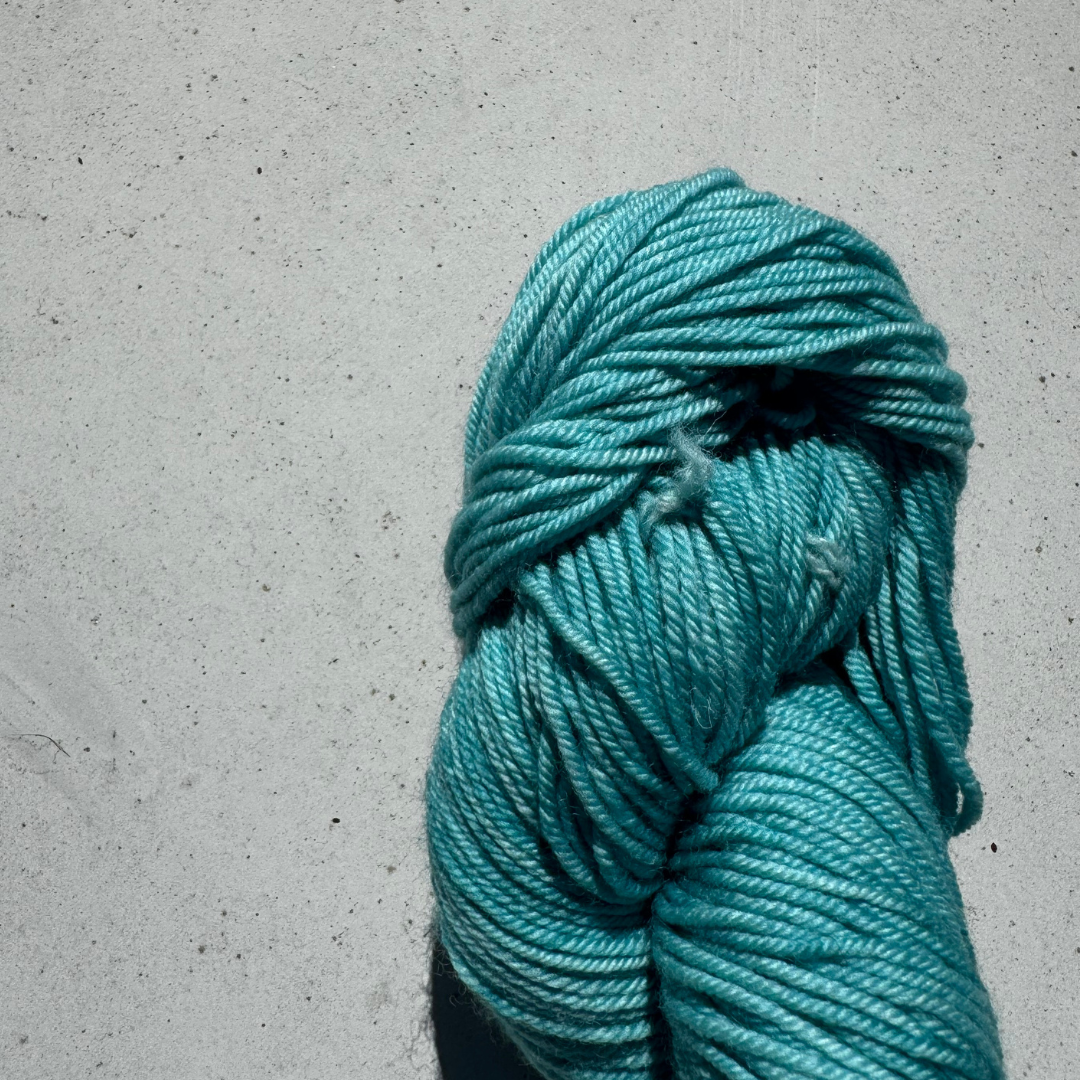Turquoise skein of yarn on a gray concrete surface