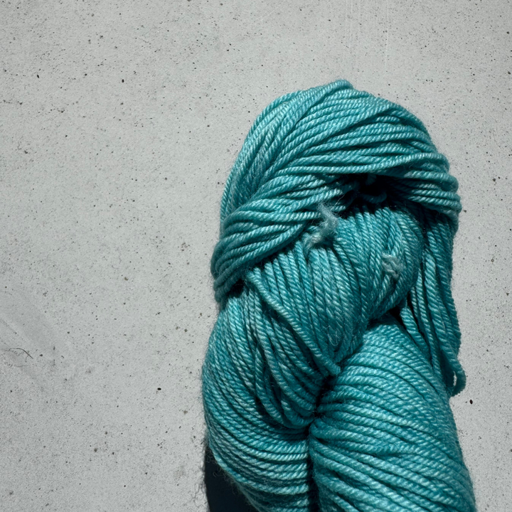 Turquoise skein of yarn on a gray concrete surface