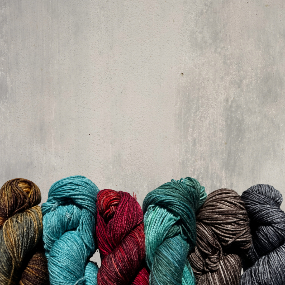 Six skeins of yarn in various colors arranged against a textured gray background