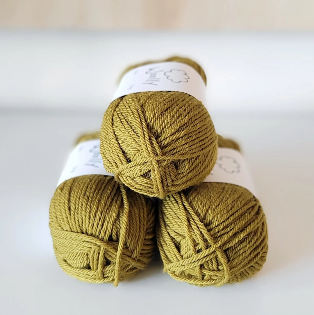 Three skeins of mustard yellow yarn stacked on a white surface