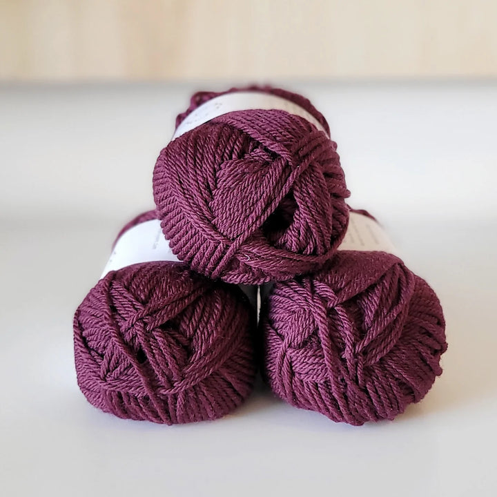 Three purple yarn balls stacked on a white surface with a beige background