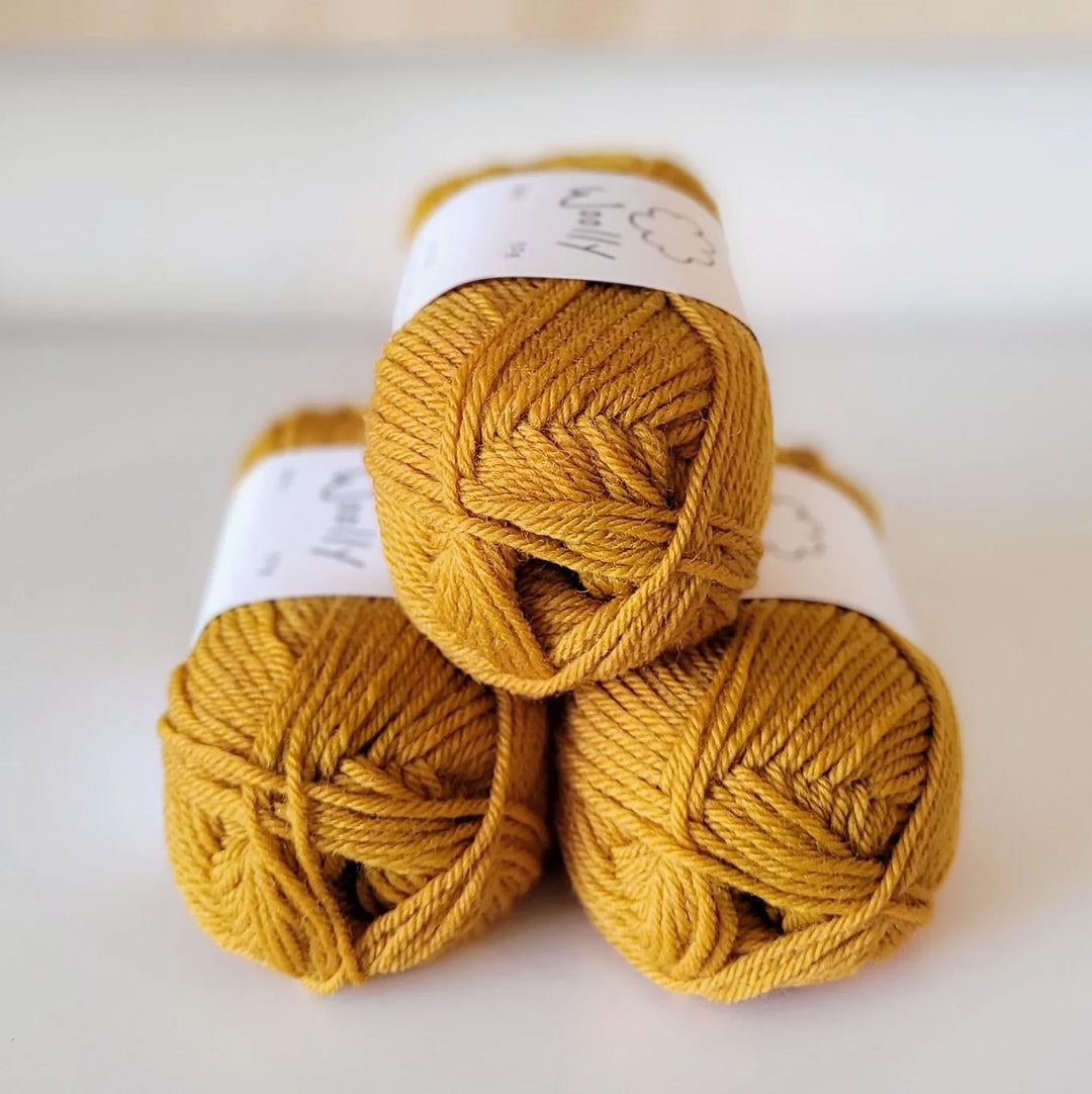 Three balls of mustard yellow yarn stacked on a white background
