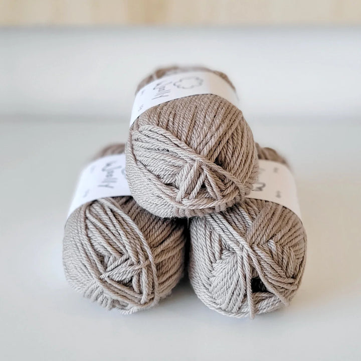 Three skeins of beige yarn stacked on a light background