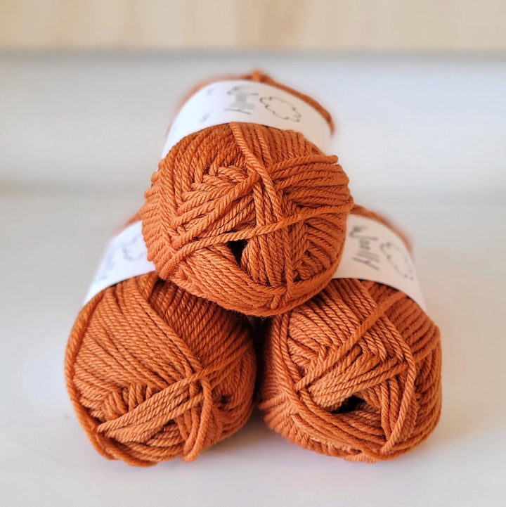 Three skeins of orange yarn stacked on a light background