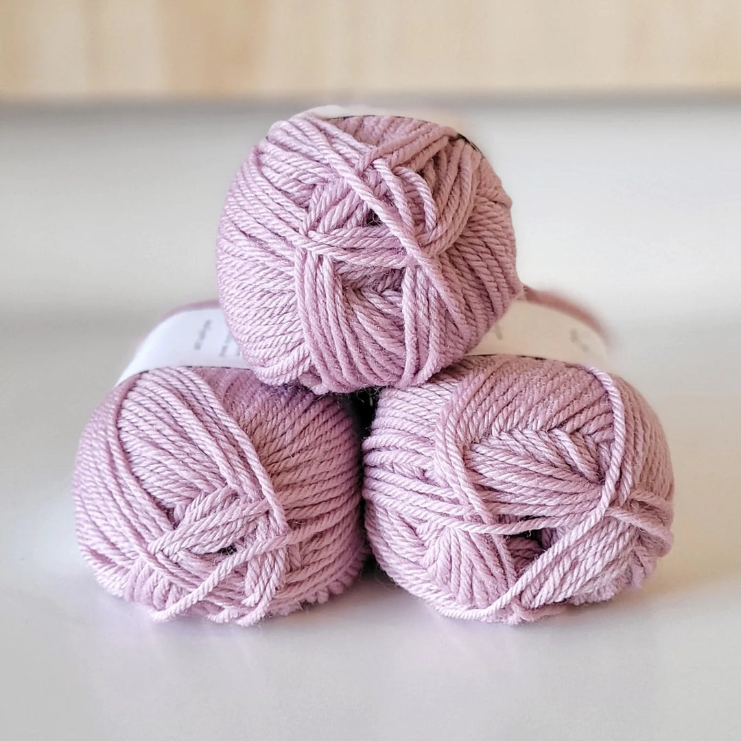 Three pink balls of yarn stacked on a light surface.