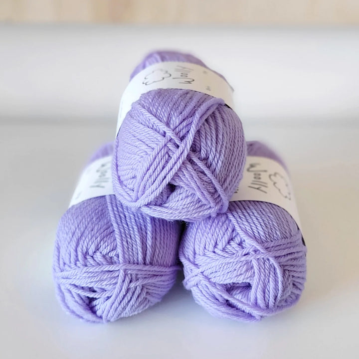Three balls of purple yarn stacked on a white surface